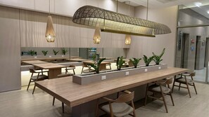 Ein moderner Essbereich mit langen Holztischen, Stühlen und hängenden Pendelleuchten.