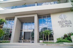 A modern building with a large glass facade, a prominent entrance with a canopy, and a sign indicating 'RESERVA DEL MAR'. - SAVIAsamaria. Confortable apartasuite con balcón y estupenda vista al mar (Santa Marta)