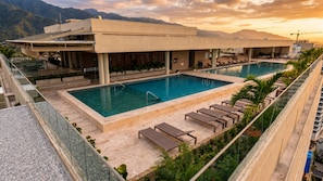 Zona de piscina con sillones de descanso, una pileta y un edificio de diseño moderno.