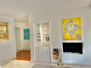 Un salon moderne avec une cheminée, des étagères blanches et des œuvres d’art.