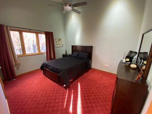 Ein Schlafzimmer mit einem Bett, einem Nachttisch, einer Kommode, einem Deckenventilator und einem Fenster mit Vorhängen.