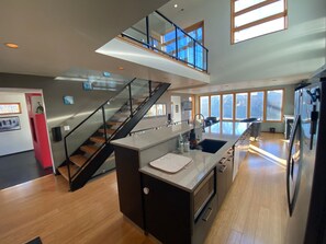 A modern kitchen with a central island, a staircase leading to an upper level, and large windows providing natural light. - Spacious 4-bedroom house in peaceful Salt Lake City with private patio (Salt Lake City)