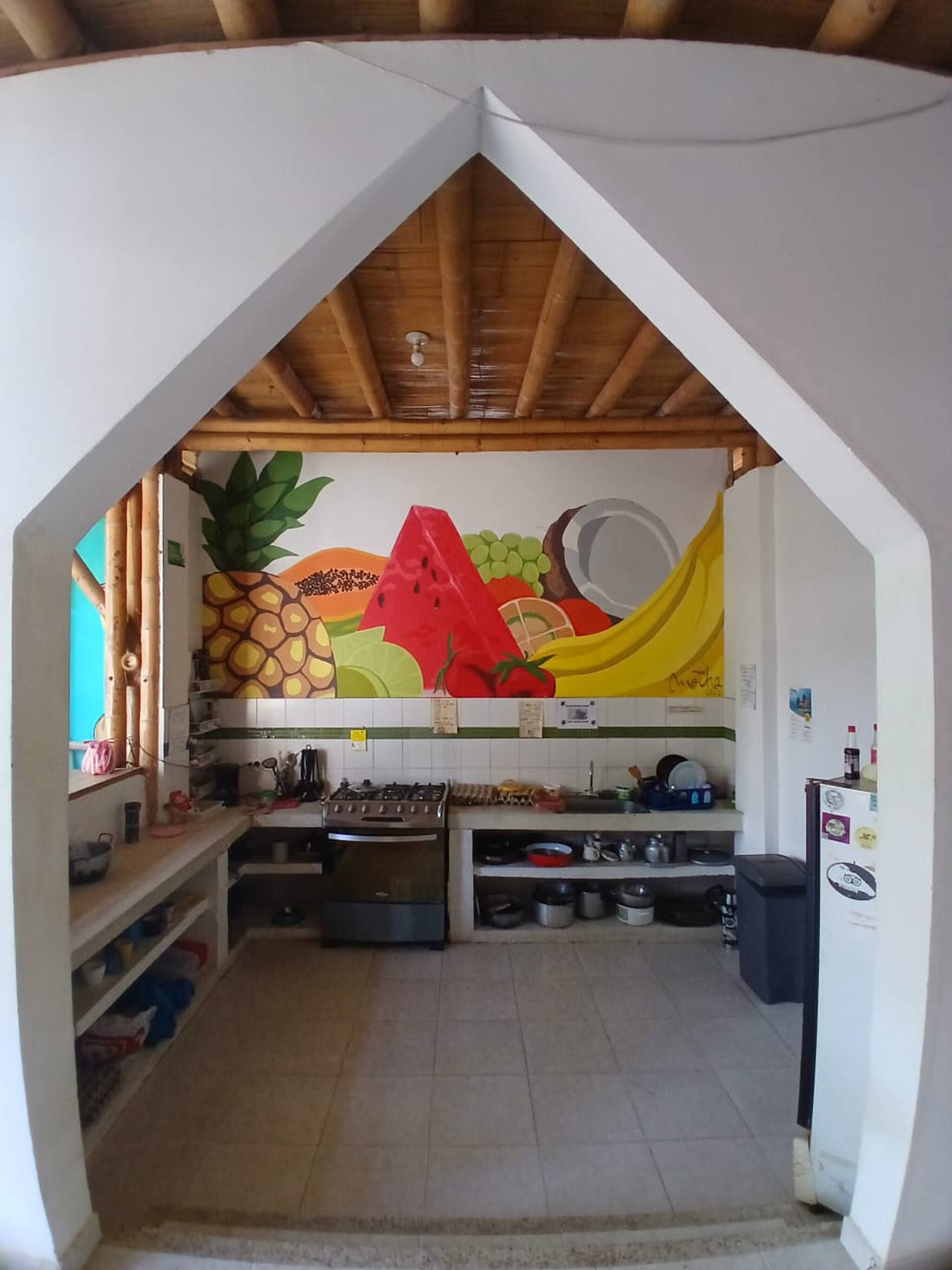 A kitchen with a wooden ceiling, a colorful fruit mural, and various kitchen appliances.
