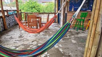 A covered outdoor area with a hammock, wooden chairs, and a concrete floor.