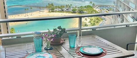 A balcony with a table set for two, overlooking a beach and ocean view.