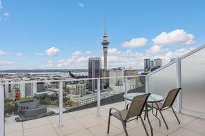 A balcony with a table and chairs, overlooking a cityscape with a prominent tower. - Top Floor Loft • 2BR/2BA • Sky Tower & Sea Views (Auckland central)