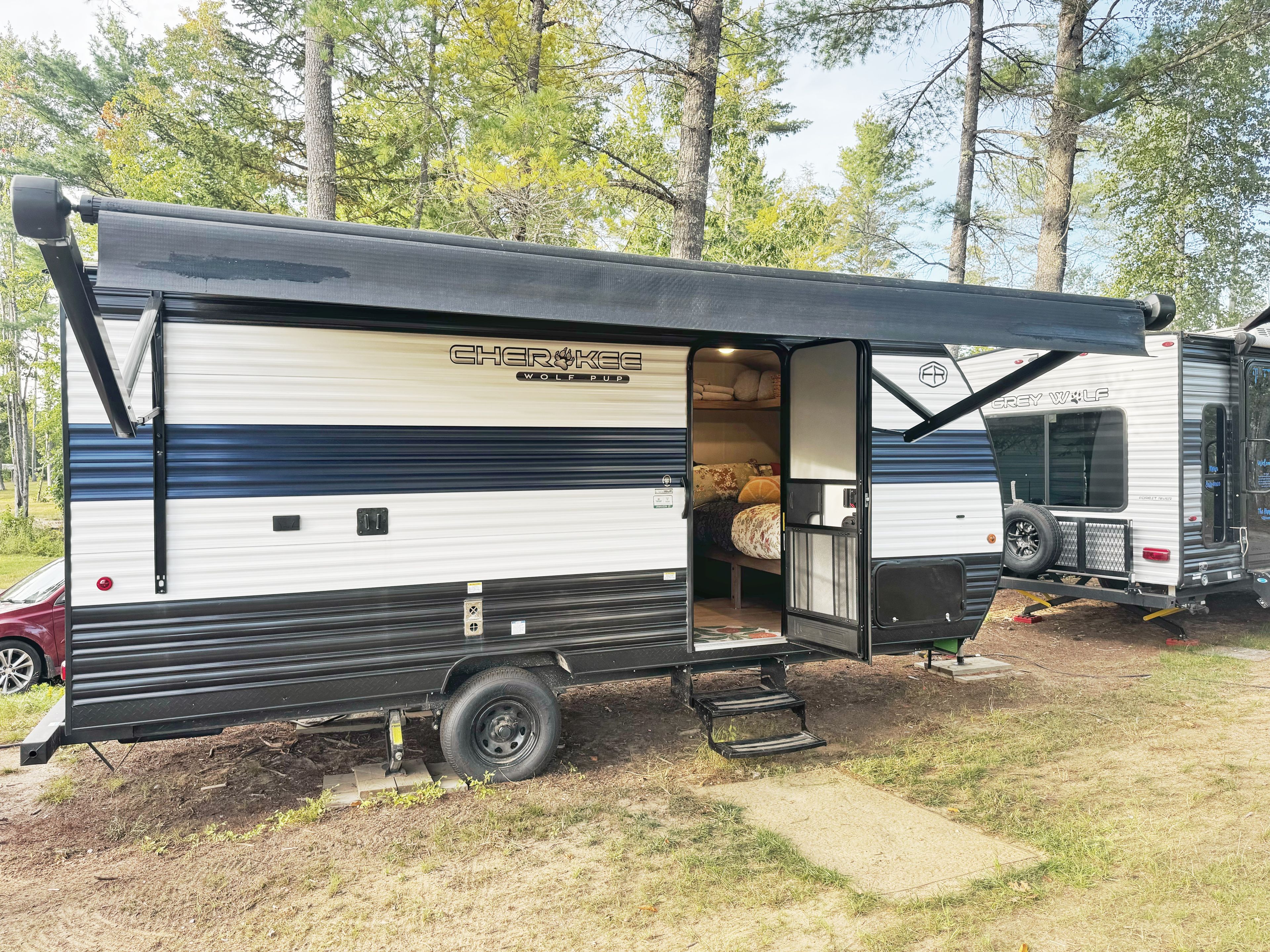 Une maison mobile dotée d’un porche couvert, d’un espace nuit avec un lit et des oreillers, et d’un petit coin cuisine.