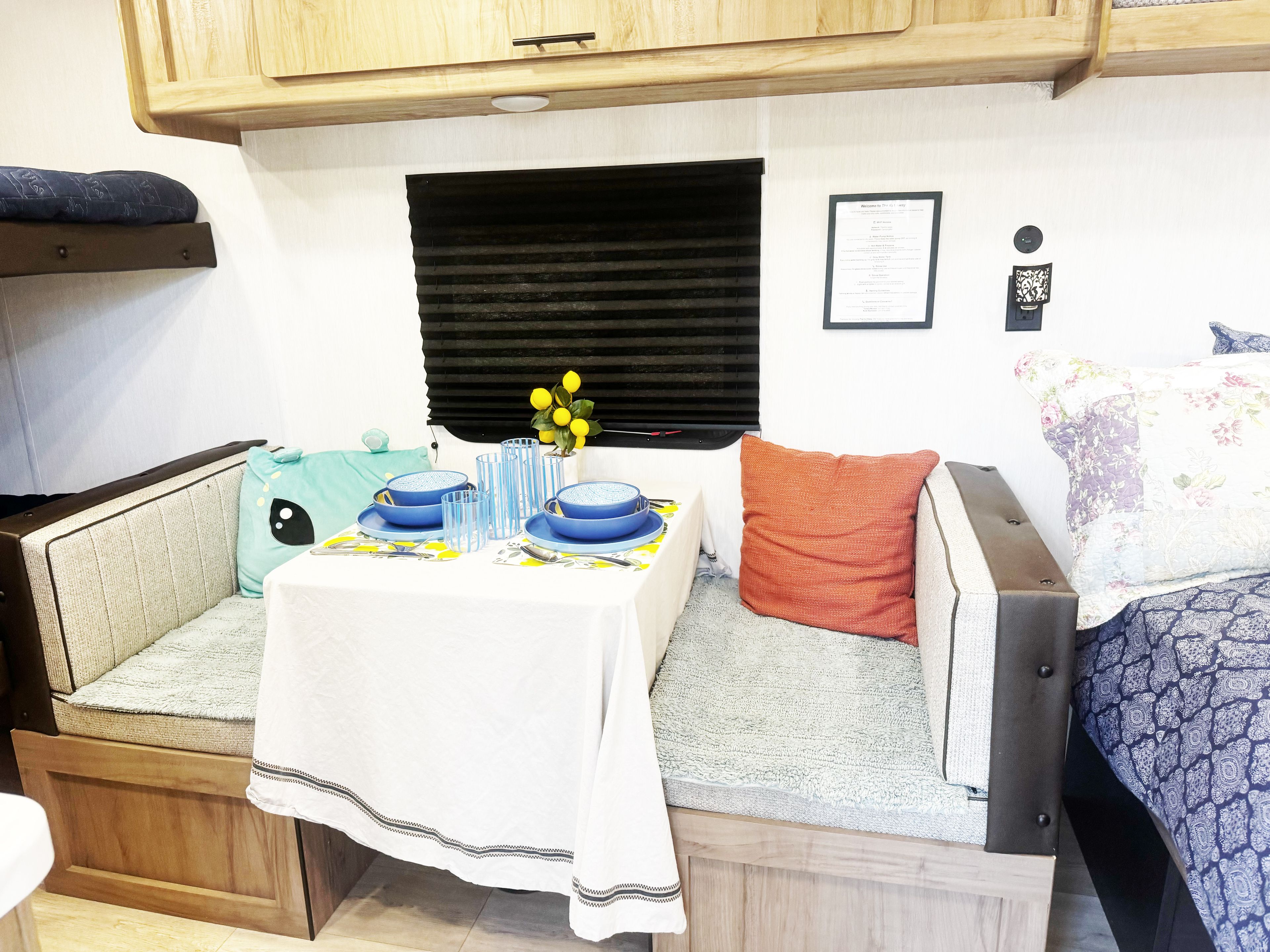 Een knus woongedeelte met een kitchenette, een eettafel gedekt met blauw servies en een bank met een bloemenkussen.