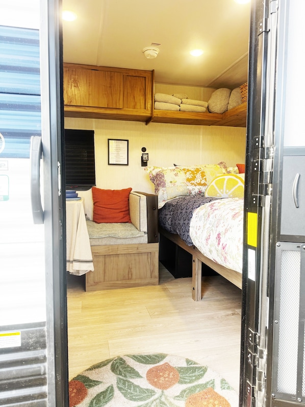 Interior compacto de una caravana con cama, zona de estar y una pequeña kitchenette.