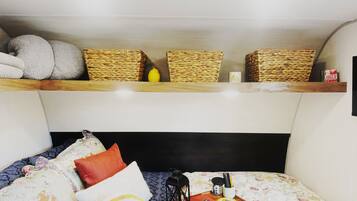 A bunk bed with a headboard, pillows, a tray with a lantern, and woven baskets on the shelf above.