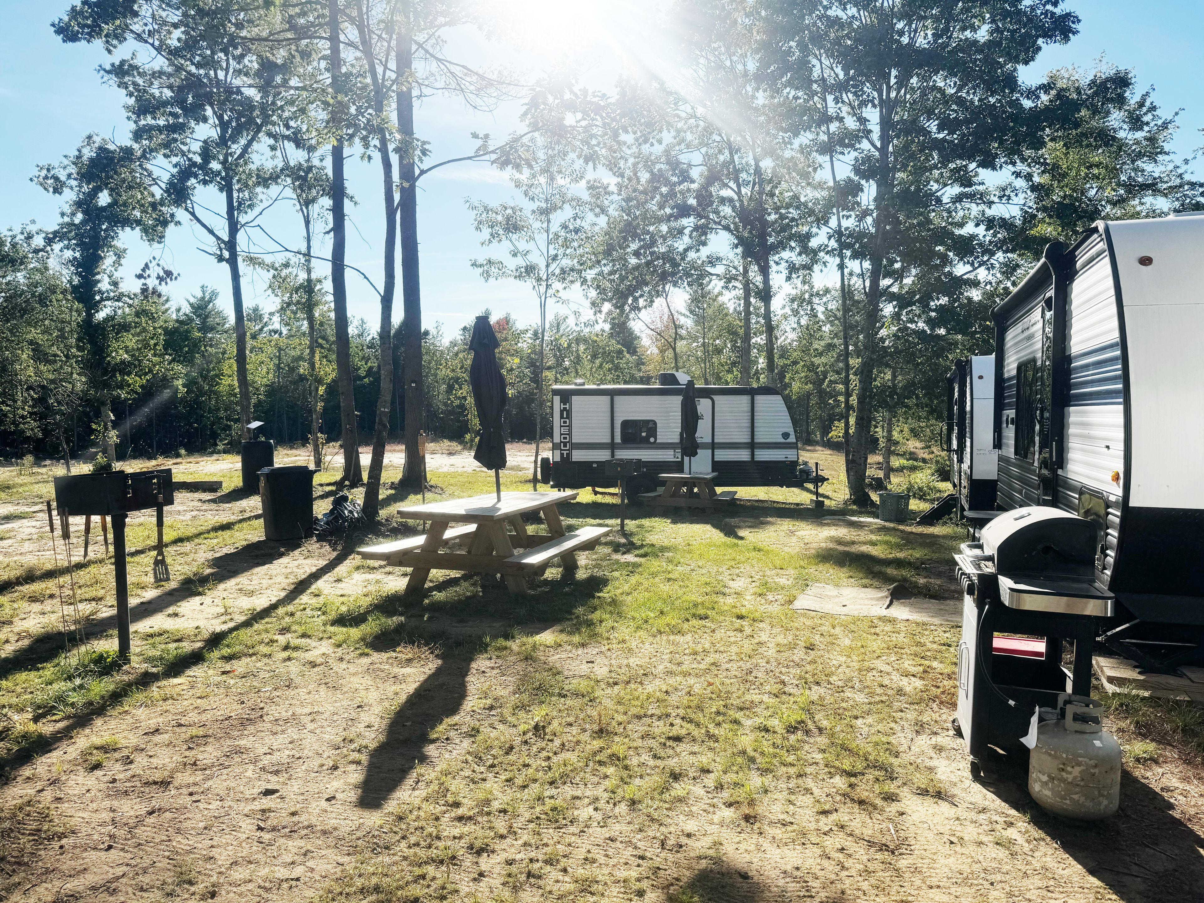 Een camping met een picknicktafel, een barbecue en een caravan.