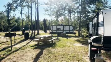 Een camping met een picknicktafel, een barbecue en een caravan.