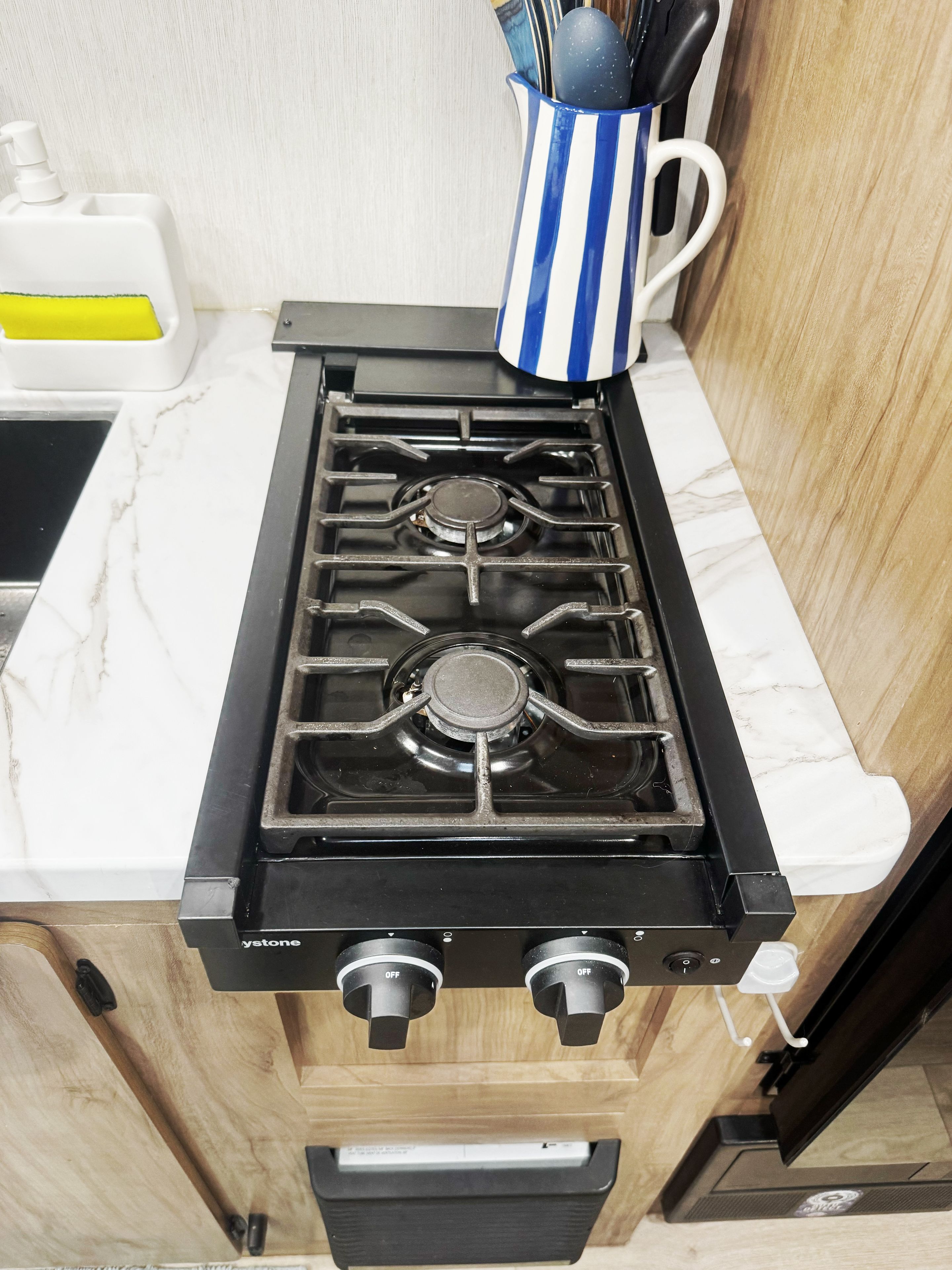 Een keuken met een zwart gasfornuis, een witte marmeren aanrechtblad en een houten kast.