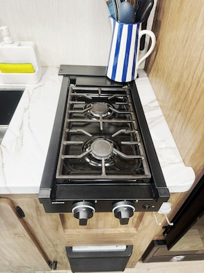 Una cocina con estufa a gas negra, encimera de mármol blanco y mueble de madera.
