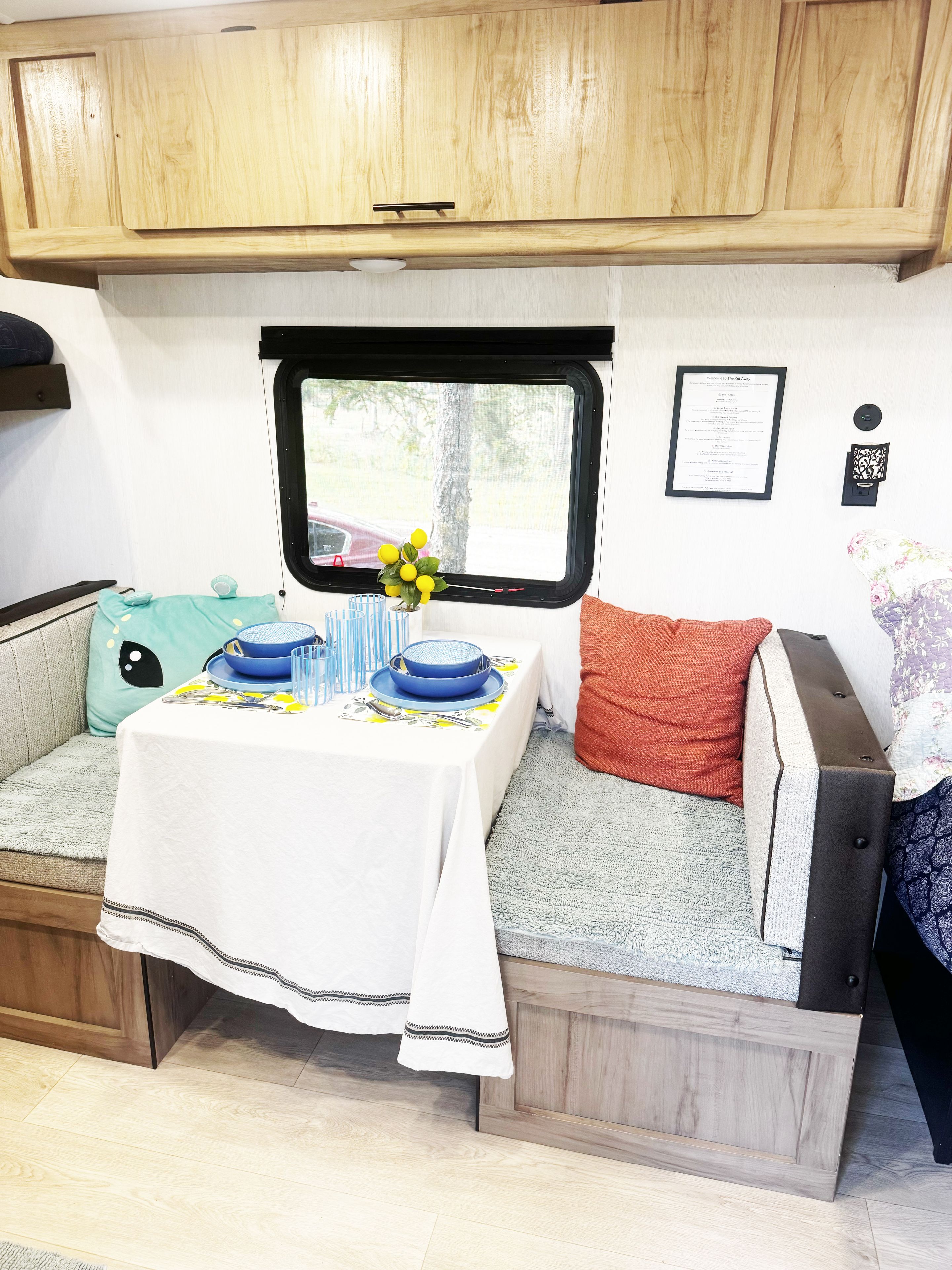 Ein kompaktes Wohnmobil-Interieur mit Esstisch für zwei Personen, einem Fenster mit Blick ins Freie und einer kleinen Sitzecke mit Kissen.