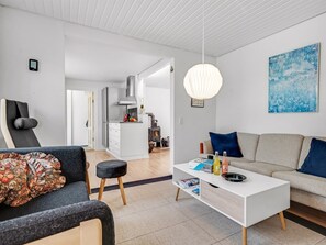 A modern living room with a sofa, a coffee table, and a chair. There is a kitchen in the background with a stove and cabinets. - "Terese" - 200m to the fjord by Interhome (Farsø)