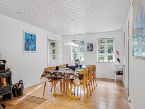 A dining area with a table set for six, wooden chairs, a stove, and a window with a view of greenery. - "Terese" - 200m to the fjord by Interhome (Farsø)