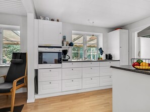 A modern kitchen with white cabinetry, a built-in microwave, a coffee maker, and a fruit bowl on the counter. - "Terese" - 200m to the fjord by Interhome (Farsø)