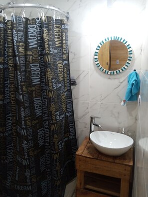 Ein Badezimmer mit Duschvorhang mit motivierenden Aufschriften, einem runden Spiegel mit Holzrahmen, einem weißen Waschbecken und einem blauen Handtuch, das an der Wand hängt.
