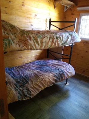 A bunk bed with floral bedding in a wooden room with a window.