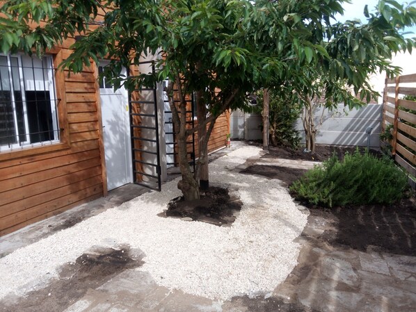 A garden area with a tree, gravel path, wooden fence, and a building with a window.