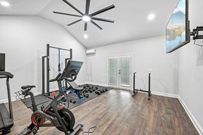 Une salle de sport à domicile équipée d’un vélo Peloton, d’un banc de musculation, d’un support à squats et d’haltères.