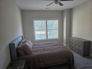 Ein Schlafzimmer mit Bett, Schminktisch, Deckenventilator und Fenster mit Jalousien.