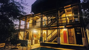 A multi-story building with a pool in the foreground, featuring outdoor stairs and a balcony.