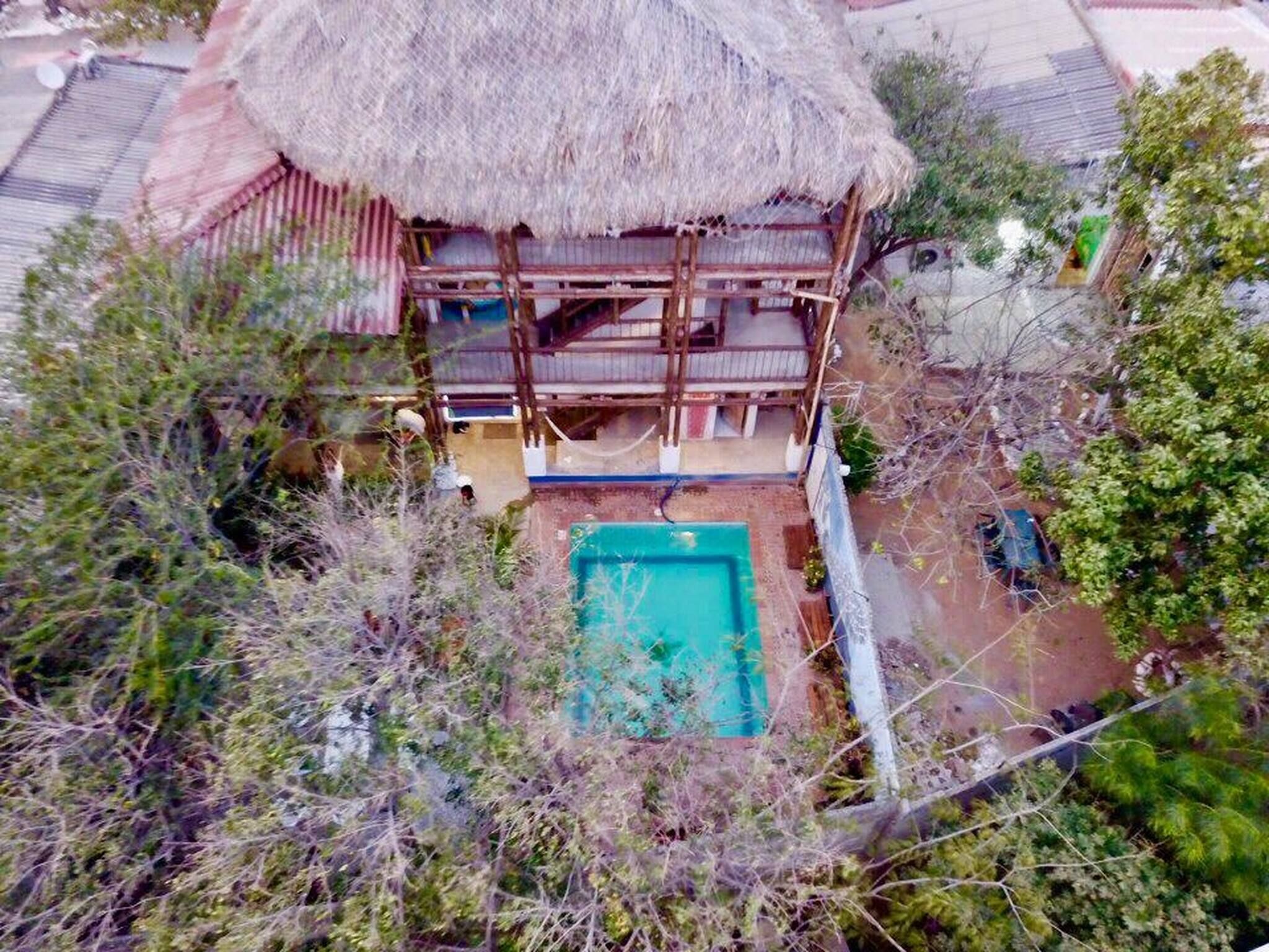 A two-story building with a thatched roof, a swimming pool, and a fenced yard.