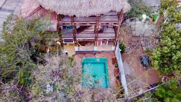 A two-story building with a thatched roof, a swimming pool, and a fenced yard.