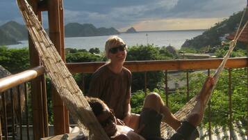 A wooden deck with a hammock, a dog, and a view of the sea and mountains.