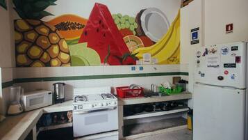 A kitchen with a gas stove, a microwave, a refrigerator, and a wall mural.
