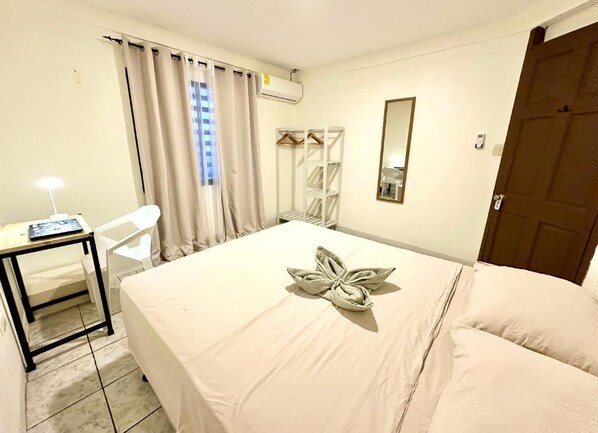 A hotel room with a bed, a desk, a chair, a wardrobe, a mirror, and a door.