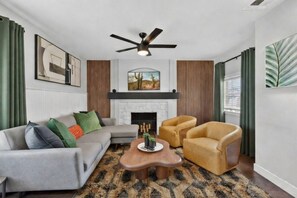 A living room with a gray sofa, two armchairs, a wooden coffee table, a fireplace, and a ceiling fan. - Mesa Harmony Haus | Bowling, Beats & Bubbles! (Mesa)