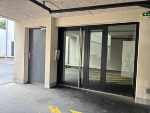 A building entrance with a glass door, a keypad lock, and a green emergency exit sign. - Á Folia - PLENEUF VAL ANDRE (PLENEUF VAL ANDRE)