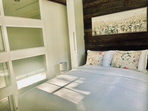 A bedroom with a bed, a nightstand, a lamp, and a painting on the wall. - Parkside Comfort Zone (Fredericton)