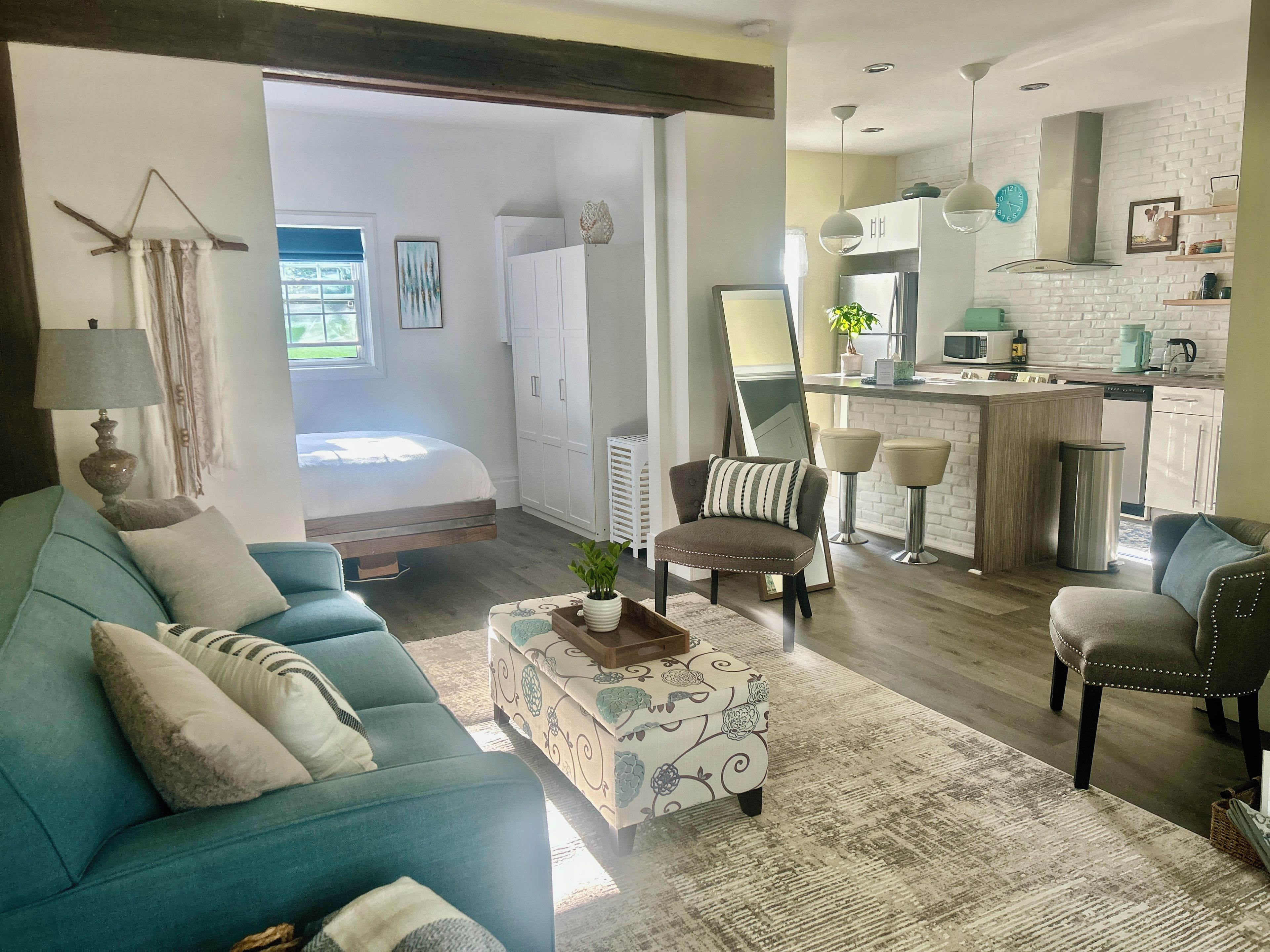 Een woonkamer met een bank, fauteuil en poef, een keuken met een centraal eiland, en een grote spiegel.