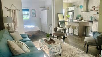 Een woonkamer met een bank, fauteuil en poef, een keuken met een centraal eiland, en een grote spiegel.