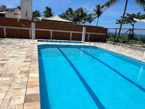 Une piscine dont le fond est recouvert de carrelage, entourée d’une clôture et de palmiers.