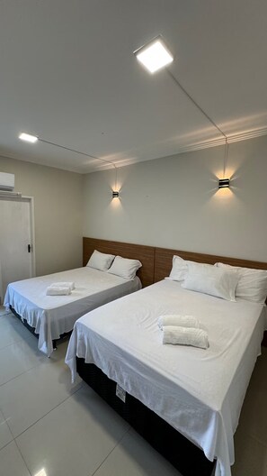 Une chambre d’hôtel avec deux lits, chacun équipé de draps et de serviettes blancs, d’une tête de lit en bois et de deux appliques murales.
