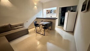 A compact living space with a sofa, a dining table with chairs, a kitchen area, and a refrigerator. - Apartment on the 1st floor facing the sea on Guaibim beach. (Guaibim)