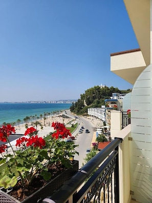 Un balcón con vistas a una carretera costera, una playa y un paisaje urbano distante.