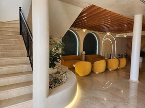 Ein modernes Interieur mit einer geschwungenen Treppe, einer Sitzecke mit gelben Stühlen und einer Holzbalkendecke.