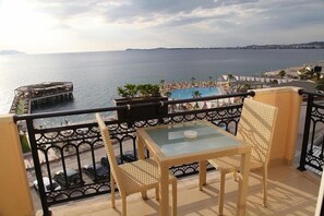 Ein Balkon mit Glastisch und Korbstühlen, der einen Blick auf ein Schwimmbecken und das Meer bietet.