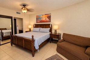A hotel room with a wooden bed, two bedside tables with lamps, a brown sofa, a large mirror, and a painting on the wall. - Sonoran Spa 707E 2 Bedroom 2 Bath (Puerto Peñasco)