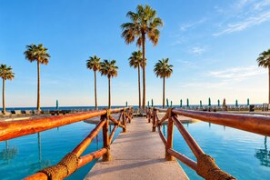 Ein Pool-Promenade mit Holzgeländer, Palmen und Liegestühlen.
