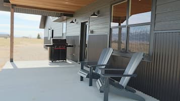 Un espace extérieur abrité, équipé d’un barbecue et de fauteuils Adirondack.