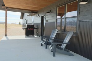 Un espace extérieur abrité, équipé d’un barbecue et de fauteuils Adirondack.