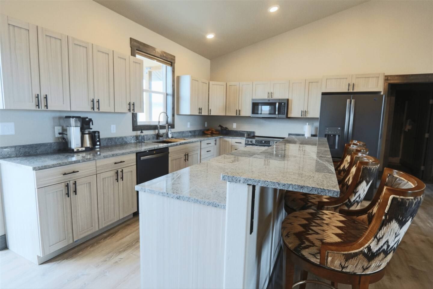 A modern kitchen with light wood cabinets, a granite countertop, and a built-in microwave.