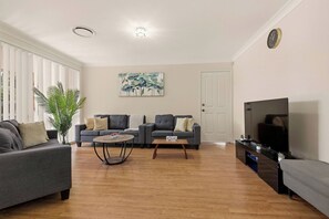 A living room with two sofas, a coffee table, a TV, and a large plant. - The Wattle House - Your Home Away From Home (Sydney)